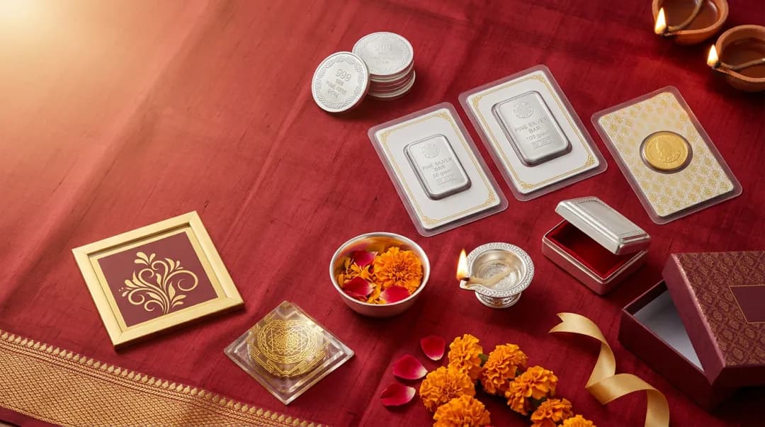 Diwali gifts laid out on red silk: silver coins and bars in sealed cards, a gold coin, a silver katori and diya, a pooja peti, a gold-foil frame, a yantra pyramid and a gift box