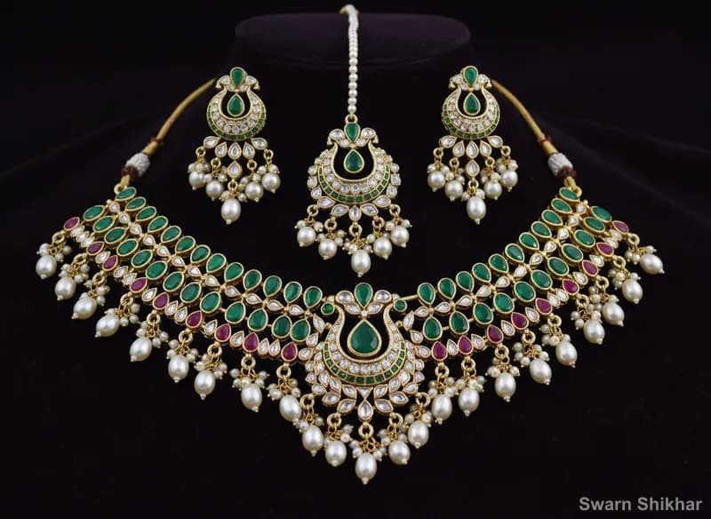 Bridal necklace set in 22K gold with matching earrings, red and green stones and pearl drops on maroon velvet