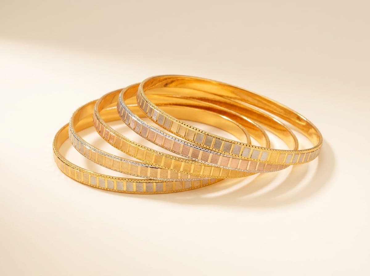 Five tri-tone Zar Serene-style gold bangles with file-cut edges, fanned on an ivory counter